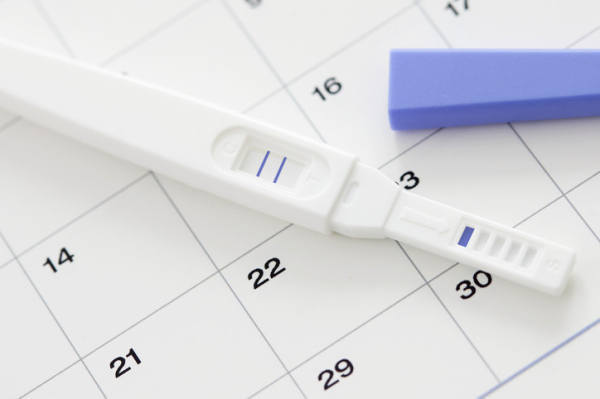 Uncapped pregnancy test showing two blue lines (positive) with blue cap nearby, arranged on a calendar